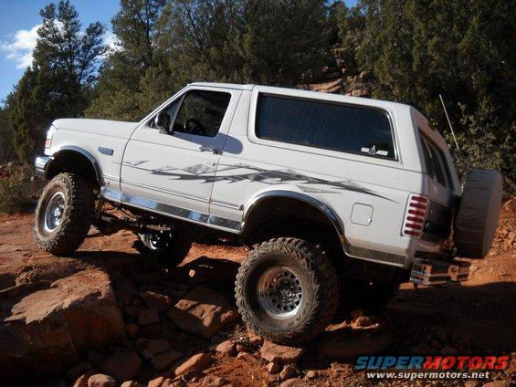 White 1996 Ford Bronco with aftermarket wheels and tires climbing over rocks
