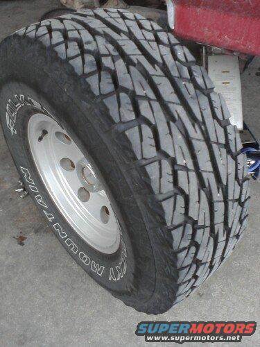 Close-up of a tire with 'SKY MOUNTAIN' text on the sidewall, mounted on a silver rim. Part of a red vehicle is visible