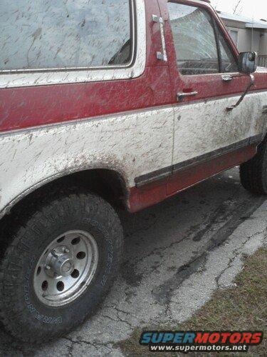 Mud-splattered red and white Ford Bronco, side view. Looks like it's from the late 80s