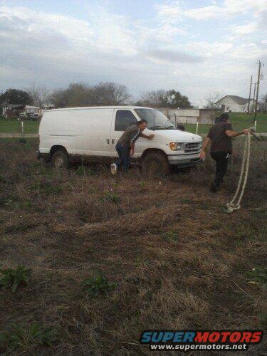 White van stuck in muddy field with two people nearby