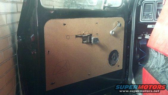 Car door panel with speaker, window crank, and cutouts for hardware. A Supermotors logo is visible