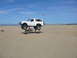 1988 Ford Bronco - White Ford Bronco performs a jump over an ATV in a desert dune area.