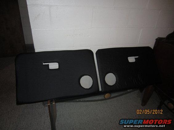 Two black door panels with circular cutouts and rectangular handle openings, resting on a metal frame
