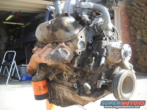 Engine on an orange stand, with an oil filter attached. A blue SUV is visible in the background