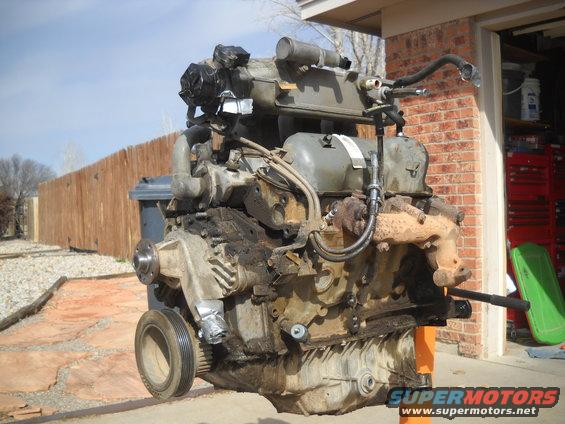 Engine on an orange stand outside a garage. It's dirty and has hoses and pipes attached
