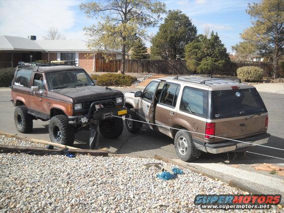 Lifted brown Bronco-like SUV with winch is parked next to a brown and tan Explorer. Both are in a driveway