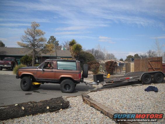 Brown Ford Bronco II towing a trailer, side view, lifted suspension, spare tire on rear