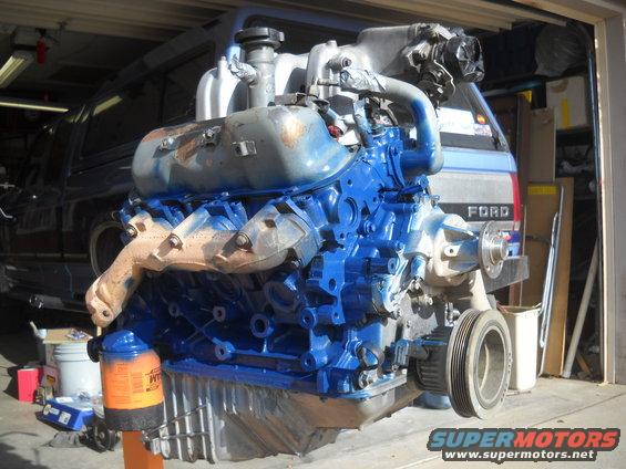 Blue painted V8 engine on an orange stand, with a Ford truck in the background
