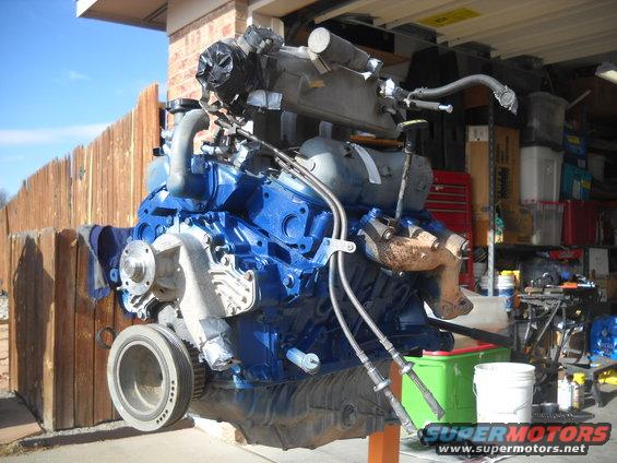 Engine assembly painted blue, mounted on an orange stand. Some parts are silver and rusty