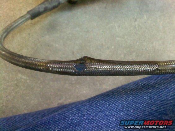 Damaged braided hose with a blue-ish hole, resting on denim