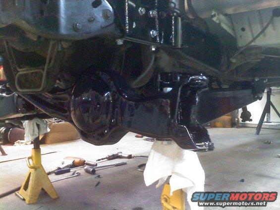 Undercarriage of a vehicle on jack stands, showing a black painted differential and suspension components