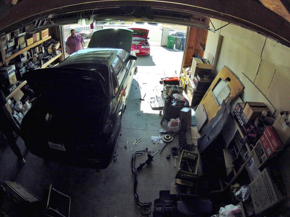 Black sedan with open trunk in garage, red car visible outside