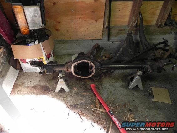 Ford rear axle assembly on jack stands with headlights and a box of parts nearby