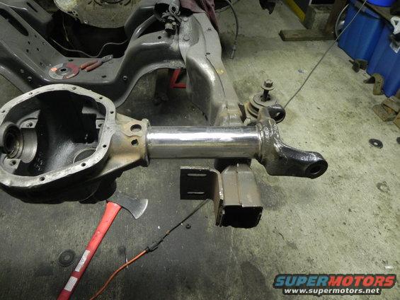 Vehicle axle housing and suspension parts on a workshop floor with an axe nearby