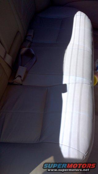 Car interior showing light-colored leather rear seats and seatbelts. A bright light casts a shadow across the seats