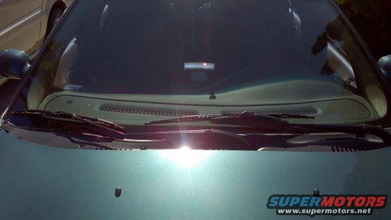 Teal car hood and windshield with sun glare, showing wipers and a small black antenna