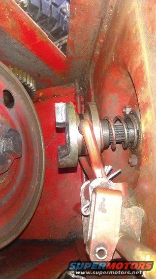 Close-up of a red mechanical assembly with a pulley, spring, and linkage. Some rust and oil are visible