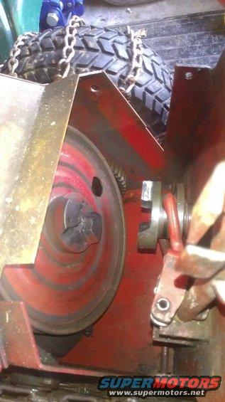Close-up of a snow blower's red auger pulley and drive mechanism, with a tire and chains visible above