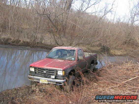 Red pickup truck stuck in muddy water, front grille visible