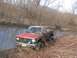 1987 Mazda RX-7 - Red pickup truck stuck in muddy water with brush on the banks.