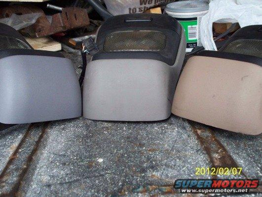 three vehicle interior console pieces, one in tan, two in gray, on a rough surface