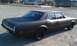 1966 Oldsmobile Cutlass - This matte black sedan is parked on a gravel lot with houses in the background.
