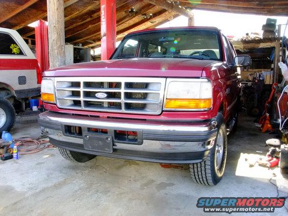 Front view of a red pickup truck with a chrome grille and bumper. Another vehicle is partially visible to the left
