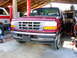 1995 Ford Bronco - A red pickup truck is parked inside a garage with another vehicle to its side.