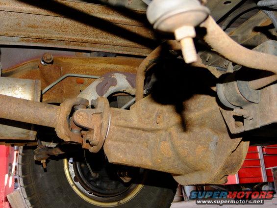Close-up of a rusty rear differential and driveshaft assembly with a tire visible