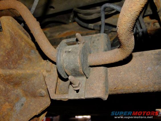 Rusty rear axle suspension bracket with rubber bushing and bolt. Wires visible above