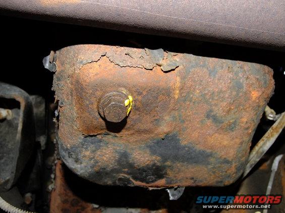 Close-up of a heavily rusted oil pan with a drain plug and yellow markings