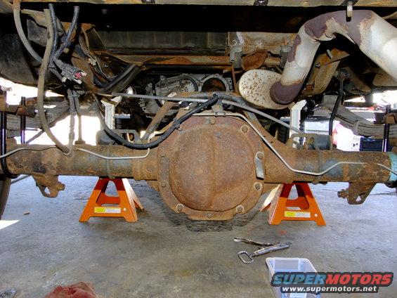 Underside of a vehicle showing the rear axle, differential, leaf springs, and exhaust system supported by jack stands