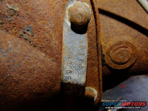 Close-up of a rusty metal tag with stamped numbers on a heavily rusted vehicle chassis component