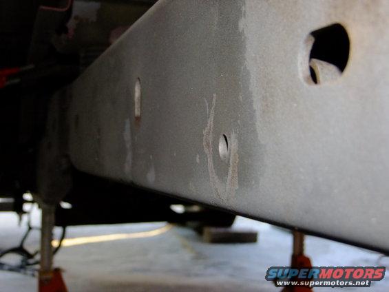 Close-up of a vehicle's metal frame rail with some rust marks and holes