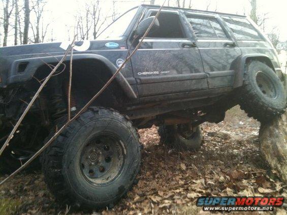 Black Jeep Cherokee Sport climbing over a rock on a wooded trail
