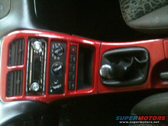 Red-trimmed car dashboard with a radio, climate controls, gear shifter, and cup holder
