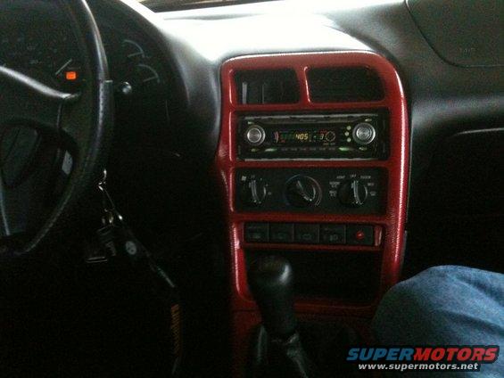 Car interior with red trim around the radio and climate controls. Steering wheel and dashboard visible