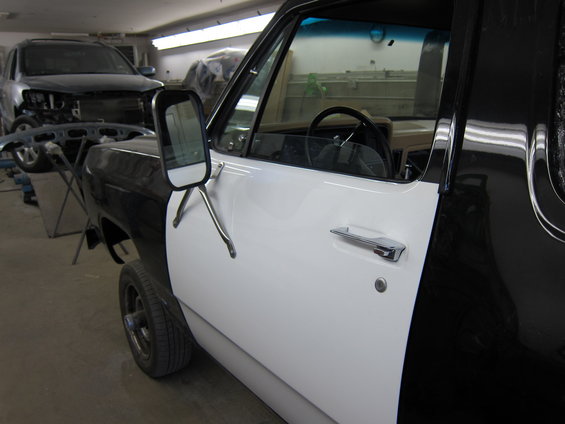 Side view of a two-tone black and white Dodge pickup truck in a shop, with another SUV in the background