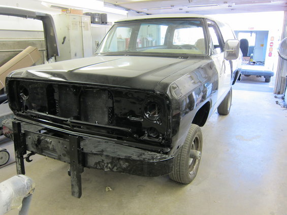 Front view of black pickup truck, undergoing bodywork. Visible grille and bumper removed
