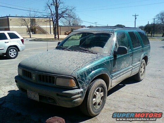 Green SUV covered in dust, front 3/4 view. License plate 957-WGT