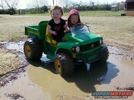 Green toy John Deere Gator with two children driving through mud puddles