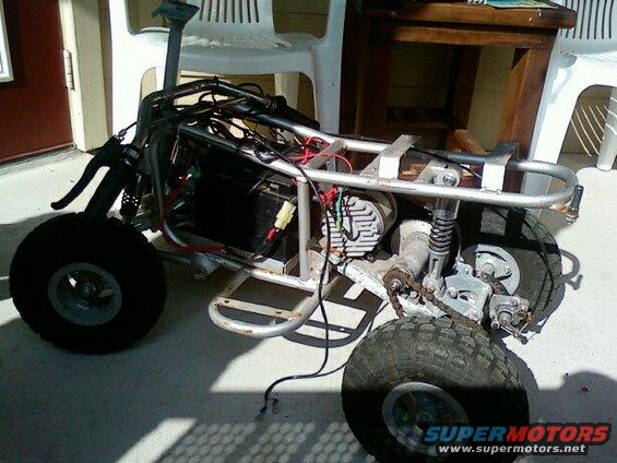 Side view of a disassembled four-wheeler with exposed wiring and engine components