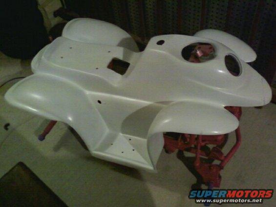 White motorcycle fairing on a red stand, showing headlight openings and mounting holes