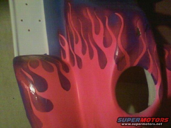 Close-up of a vehicle fender with pink and purple flame graphics. There's a circular cutout visible