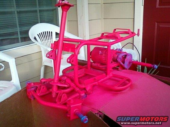 Go-kart frame painted bright pink, with engine attached. Sitting on cardboard