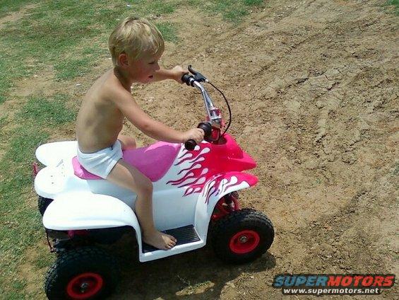 Kid riding a pink and white toy ATV with flame decals