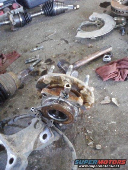 Disassembled vehicle hub assembly and CV axle parts on a garage floor