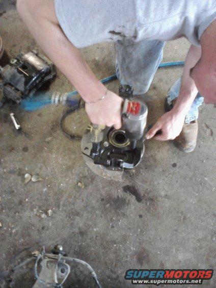 Guy using impact wrench on a brake caliper assembly. Another part is on the floor