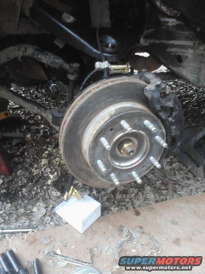 close-up of a vehicle's rear brake rotor and caliper assembly, with lug nuts visible