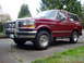 1993 Ford Bronco - A red Ford Bronco is parked on a driveway next to another vehicle, with trees in the background.